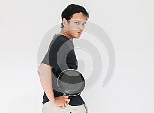 Young Asian man is angry and ready to strike with a frying pan. Indonesia Man wear black shirt Isolated grey background