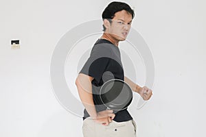 Young Asian man is angry and ready to strike with a frying pan. Indonesia Man wear black shirt Isolated grey background