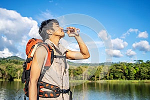 Young Asian man backpacker traveling in the forest. Male traveler holds a bottle of water. Healthy hiker drinking water in nature