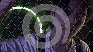 Young Asian man behind a wire mesh or fence. Stylish Asian man looks through a metal barrier