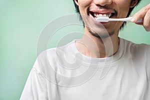 Young asian man brushing teeth with a pink toothbrush wear white t-shirt in morning on green background