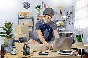 Young Asian man business owner working at home Start up for Business Online, working with laptop for checking, packaging delivery