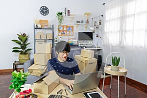 Young Asian man business owner working at home Start up for Business Online, working with laptop for checking, packaging delivery