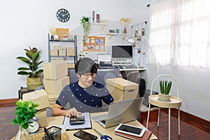 Young Asian man business owner working at home Start up for Business Online, working with laptop for checking, packaging delivery