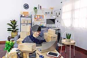 Young Asian man business owner working at home Start up for Business Online, working with laptop for checking, packaging delivery