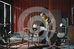 Young Asian man Carpenter uses a tape measure to measure chair on the workbench in woodcraft carpentry workshop.