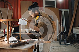 Young Asian man Carpenter uses a tape measure to measure chair on the workbench in woodcraft carpentry workshop.