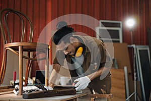 Young Asian man Carpenter uses a tape measure to measure chair on the workbench in woodcraft carpentry workshop.