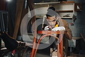 Young Asian man Carpenter uses a tape measure to measure chair on the workbench in woodcraft carpentry workshop.