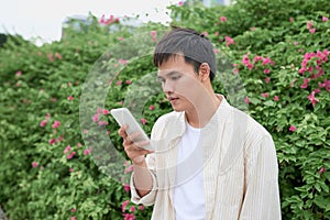 Young asian man in casual clothes on summer day and using smartphone for sending sms