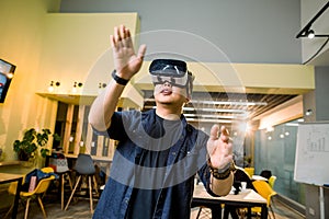 Young asian man in casual clothes wearing head-mounted virtual reality goggles. Man with vr glasses posing in modern
