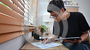 Young asian man checking stock market data on tablet.