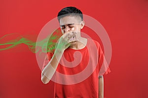 Young Asian man close his nose for bad smell, on red color