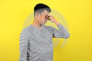 Young Asian man close his nose for bad smell, isolated on yellow