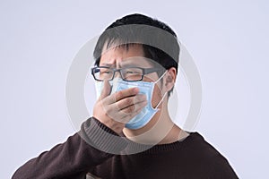 Young Asian man is coughing, feeling unwell, vomit sick with wearing a medical blue face mask isolated on white background, close