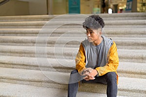 Young Asian man with curly hair sitting on staircase in the city