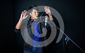 Young asian man dance, swaying, and lifting his arms rhythmically while singing in front of black soundproofing wall. Musician