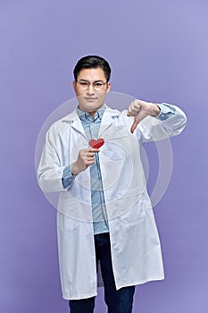 young Asian man doctor holding red heart and giving thumb down