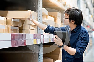 Young Asian man doing stocktaking by using tablet in warehouse