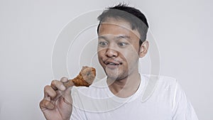 Young Asian man is eating fried chicken wear white shirt feeling tempted and hungry