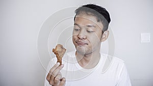 Young Asian man is eating fried chicken wear white shirt feeling tempted and hungry