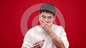 Young asian man eating red hot chilli peppers against red studio background. Crying, spicy hot taste. Burning mouth