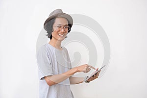 Young asian man with fedora hat and glasses using tablet and smiling