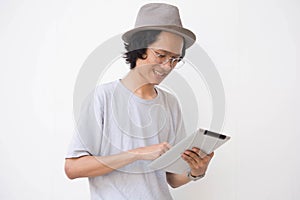 A young asian man with fedora hat and glasses using tablet and smiling