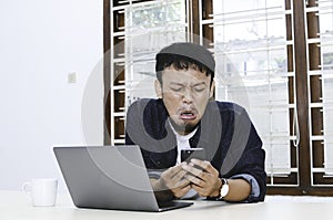 Young Asian man feeling sad when work laptop and phone on table