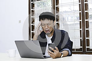 Young Asian man feeling sad when work laptop and phone on table