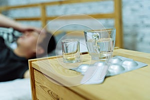 Young Asian man feeling sick and ill lying on bed with medicines tablets and pills on table