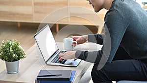 Young asian man freelancer working online with computer laptop while sitting on sofa at home.