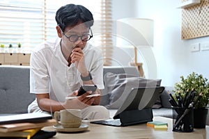 Young asian man freelancer working online at home with computer tablet and using smart phone