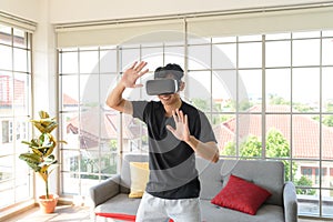 Young Asian man getting experience with VR virtual reality headset or 3D glasses in living room at home. technology, gaming