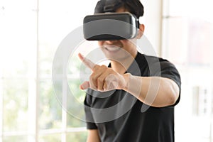 Young Asian man getting experience with VR virtual reality headset or 3D glasses pointing with his finger in living room at home.