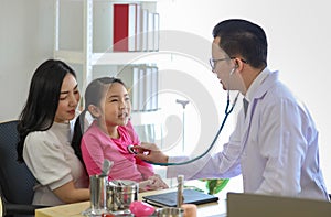 Young Asian man in glasses with stethoscope clecking and examinate by  listening to heartbeat of little girl sitting with mother