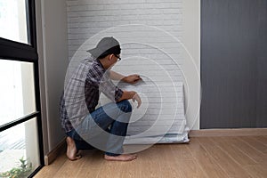 Young Asian man glueing wallpapers on the wall at home.