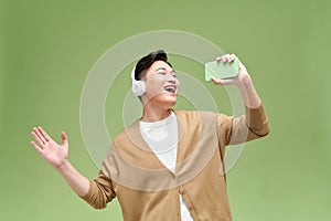 Young Asian man happily sings his favorite song. He is holding a smartphone