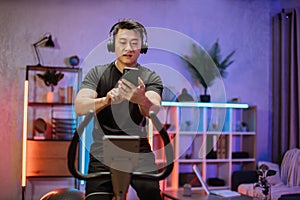 Young asian man with headphones doing exercises on stationary bicycle at home or fitness center.