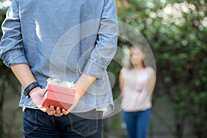 Young asian man holding behind back gift box surprise girlfriend excited in the garden with happy, anniversary day of couple