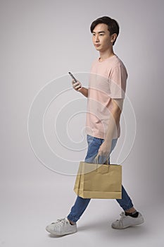 Young asian man holding smartphone and shopping bag over white background studio, shopping and finance concept