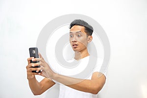 Young asian man holding smartphone and surprised by notification on his smartphone about discount or cash back from online shop