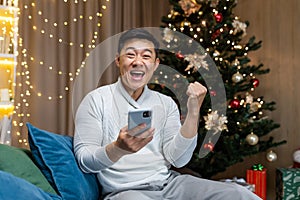 A young Asian man holds the phone in his hands, rejoices at the Christmas win in the raffle