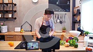 Young asian man in kitchen recording video on camera. Smiling asian man working on food blogger concept with fruits and vegetables