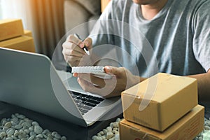 Young asian man looking on computer laptop and writing order list on paper, SME concept