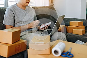 Young asian man looking on computer laptop and writing order list on paper, SME concept