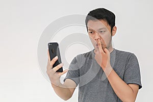 Young Asian man looking in the smartphone with nose picking gesture