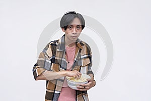A young asian man looking spooked while holding a bowl of popcorn. Isolated on a white background