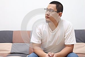 Young Asian man looking up and thinking, contemplation gesture, while sitting on sofa