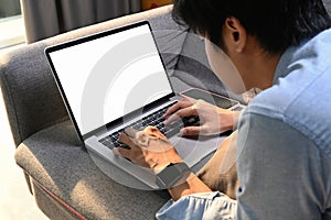 Young man lying on comfortable sofa at home and browsing internet on laptop computer.